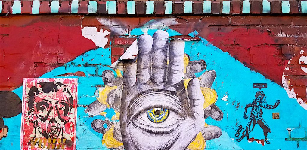 Art on a wall with an eye in the palm of a hand.